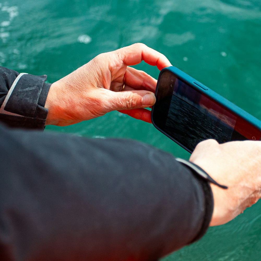 Hände halten ein Smartphone über grünem Wasser